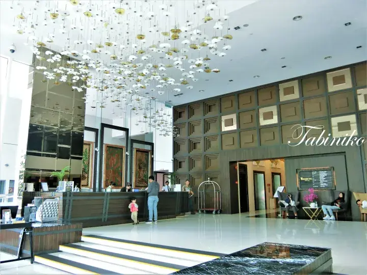 Elegant hotel lobby with a grand chandelier, reception desk, and a wall featuring the name Tabiniko.