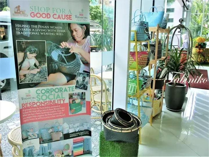 Verdant Hillのペナン女性プロジェクトのCSRバナーと色とりどりの織りバッグの展示。