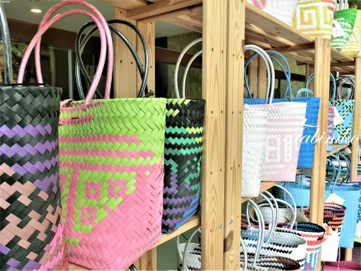 Colorful woven tote bags with geometric patterns displayed on wooden shelves in a boutique.