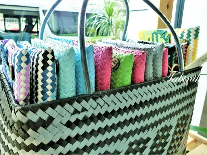Colorful woven wallets displayed in a large black and white basket at a market stall.