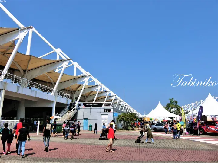 Crowd walking outside the modern white steel structure of Sunway Pyramid under a clear blue sky.