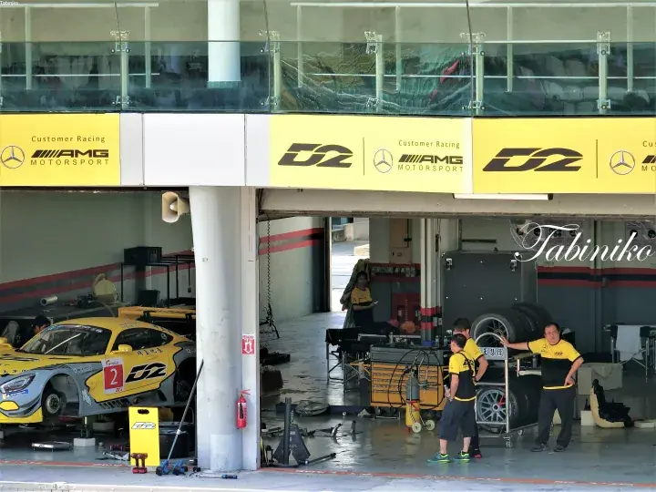 AMG Motorsport garage with D2 branding and a yellow race car being serviced by mechanics.