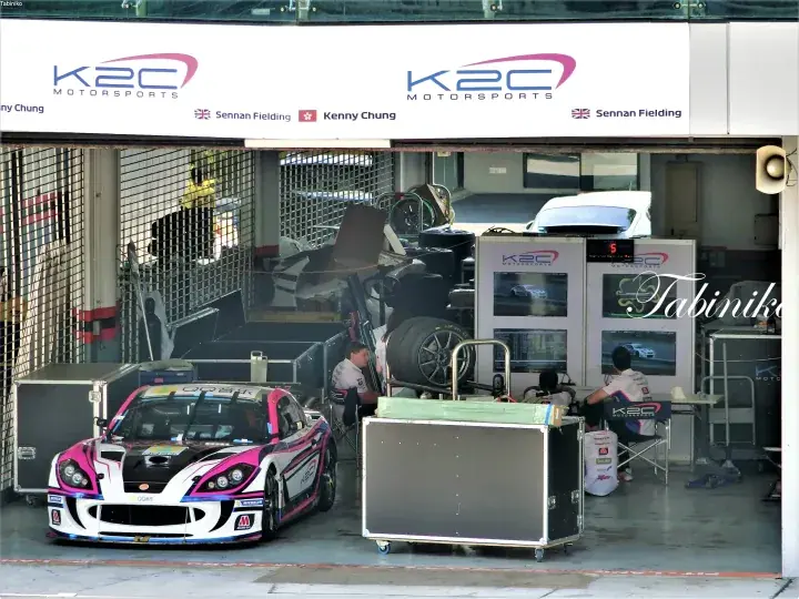 K2C Motorsports garage with a pink and white race car and team members working inside.