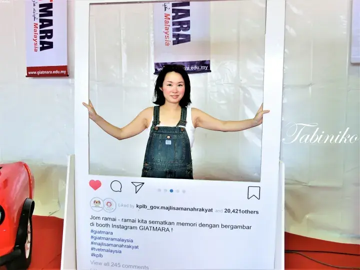 Woman posing inside a GIATMARA Instagram booth frame at an event.