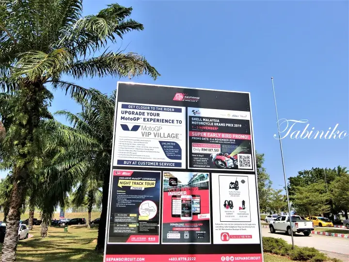 Sepang Circuit signboard advertising MotoGP VIP Village and Shell Malaysia Motorcycle Grand Prix 2019 under a blue sky.