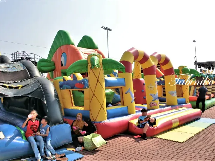 Colorful inflatable bouncy castle with palm tree design at an outdoor playground where children and adults are playing and relaxing.