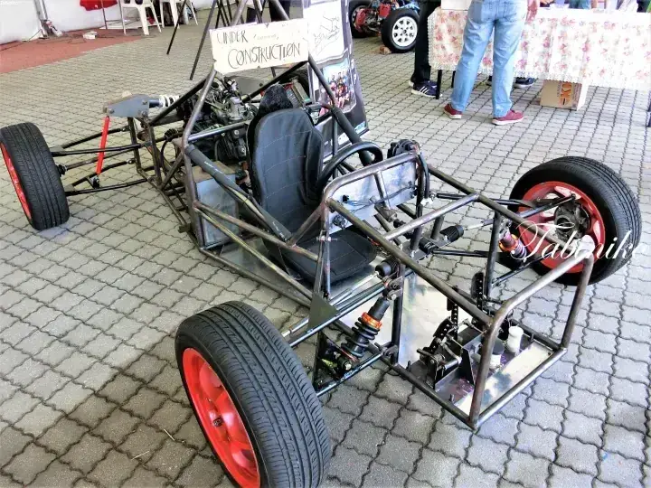 赤いホイールと黒いシートを備えたカスタムゴーカートシャーシが屋内展示会で展示されている。