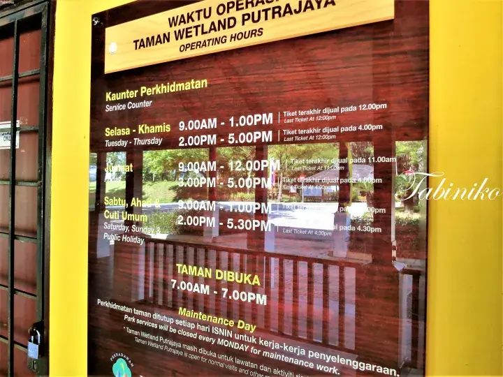 Operating hours sign for Taman Wetland Putrajaya showing service counter times and park opening hours.