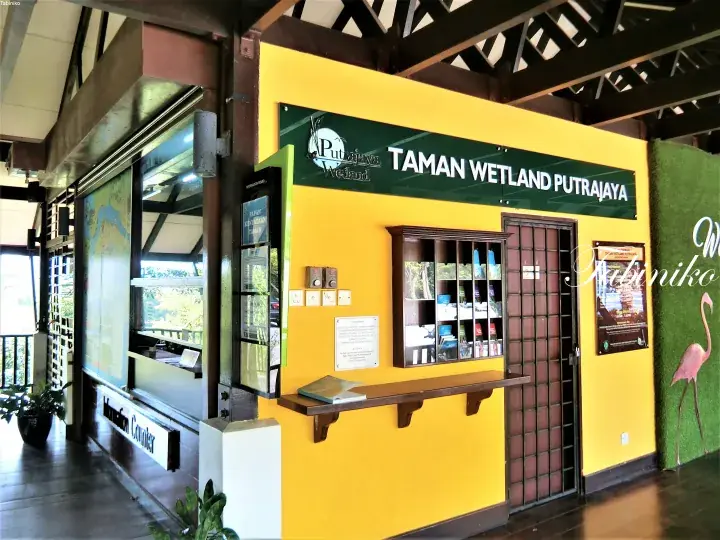 The vibrant yellow ticket counter and brochure display at the entrance of Taman Wetland Putrajaya visitor center.