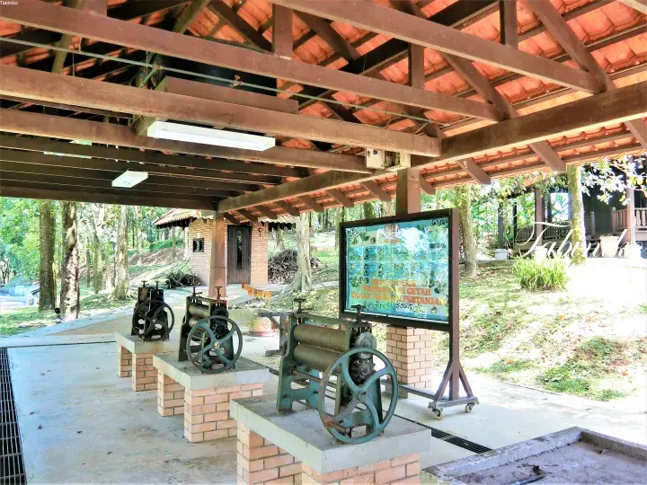 Vintage rubber processing machinery displayed under a wooden shelter at a heritage site in Malaysia.
