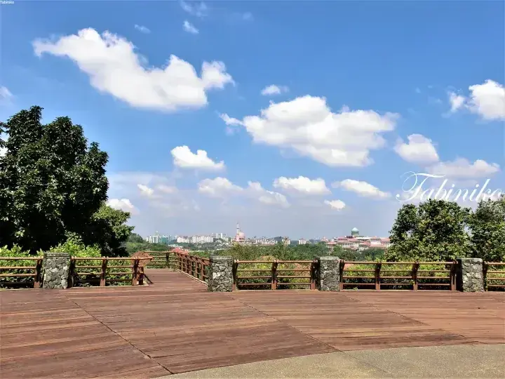 青空と白い雲の下、街並みを一望できる石造りの柱がある木製の展望デッキ。