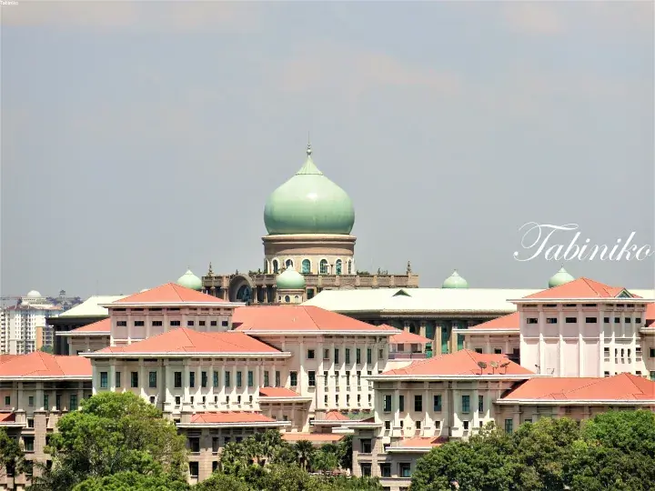 The Putra Mosque in Putrajaya, Malaysia, featuring its iconic green dome and red-tiled roofs against a clear sky.