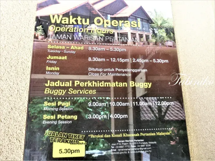 Signboard showing operation hours and buggy service schedule at Taman Warisan Pertanian in Malaysia.