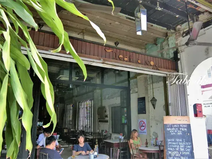 大きな緑の葉に囲まれ、木製の看板が目印のLeaf & Coカフェの外観と客席。