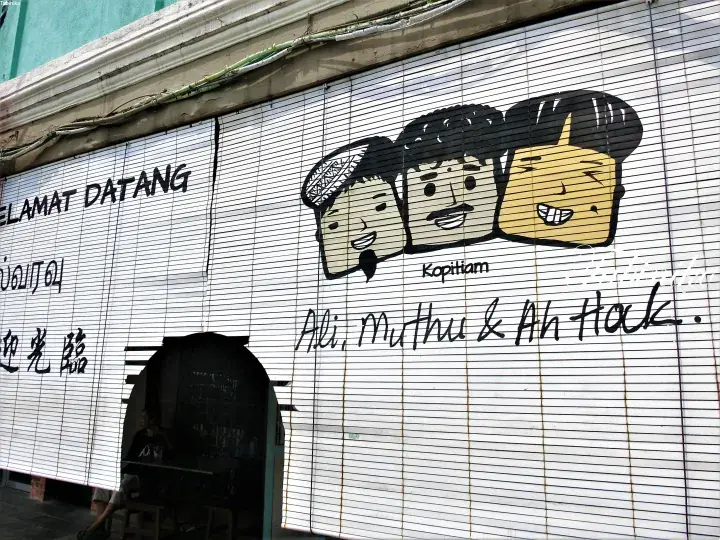 Mural of Ali, Muthu & Ah Hock faces on a shop front with ‘Selamat Datang’ welcome text.