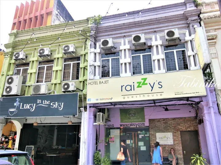 Street view of Hotel Bajet and Raizzy’s Guesthouse in Malacca, featuring colorful shophouses and Lucy in the Sky cafe.