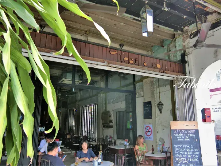 Leaf & Co cafe exterior with patrons dining under large green leaves and rustic wooden signage.