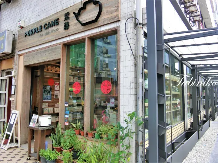 Purple Cane tea shop exterior with wooden signage, large glass windows, and potted plants on the sidewalk.