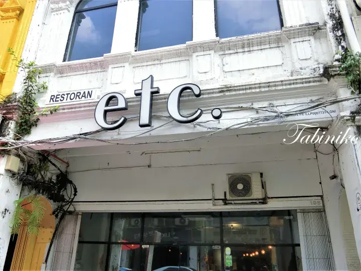 Exterior of RESTORAN etc. cafe with white facade, large windows, and hanging vines in a heritage building.