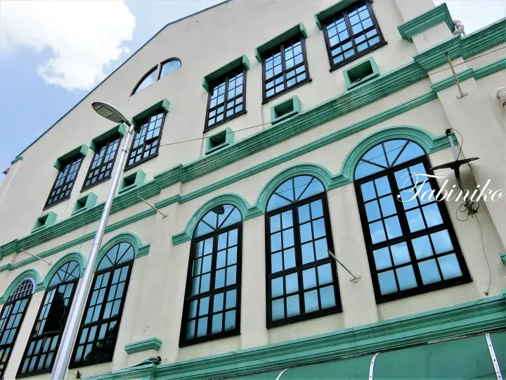 Cream building with green trim and arched windows, featuring the Tabiniko watermark on the facade.