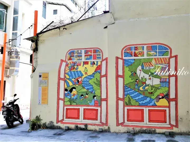マレーシアの街角に描かれた、川沿いの風景を表現したカラフルな壁画。手前にはバイクが駐車されている。