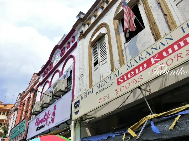 Traditional shophouses with a Malaysian flag and a sign for Siew Kum Hor Foods in Malaysia.