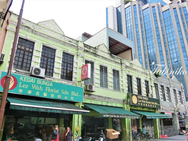 Green heritage shophouse housing Lee Wah Florist Sdn Bhd with modern skyscrapers in the background.