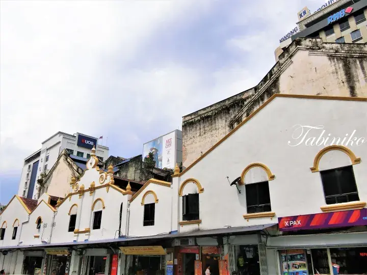 Traditional white shophouses with gold trim and X-PAX signage in a Malaysian city street.