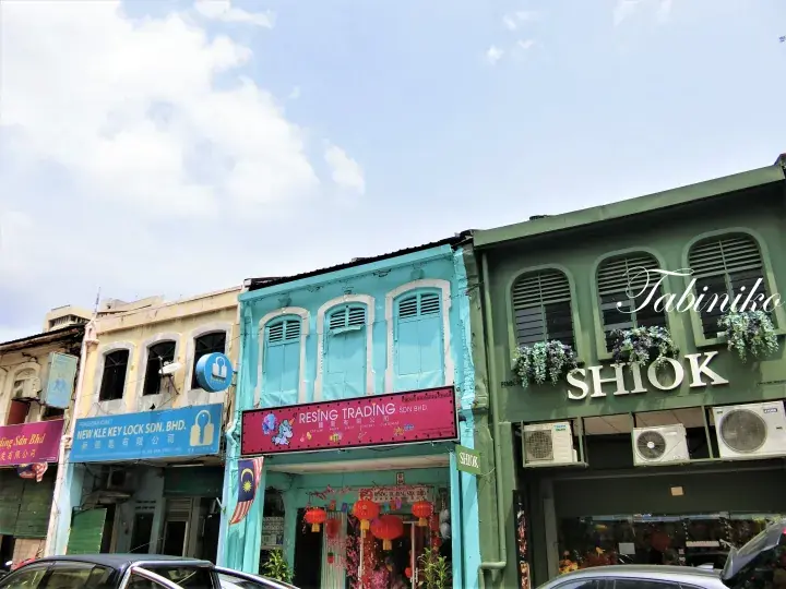 Colorful heritage shophouses in Malaysia featuring Resing Trading and Tabiniko SHIOK under a bright sky.