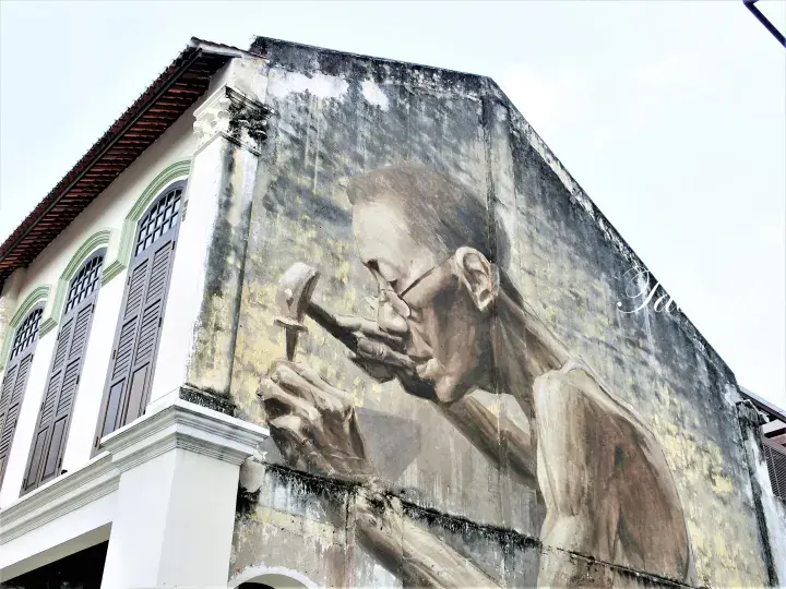 Large mural of a craftsman painting on a heritage shophouse wall in George Town, Penang, Malaysia.