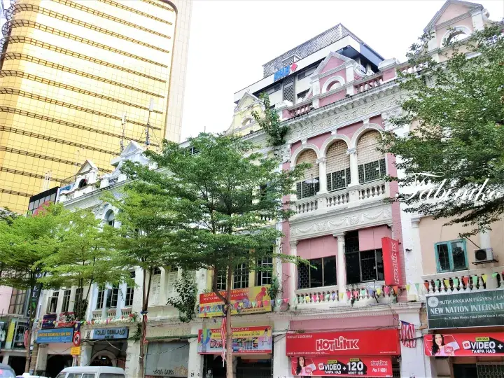 Colorful shophouses with Hotlink signage stand beside a modern gold skyscraper in a bustling Malaysian city street.