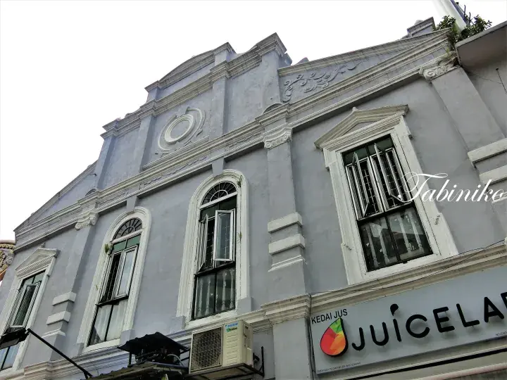 Grey colonial shophouse facade with ornate details and a Juicelab juice shop sign on the ground floor.