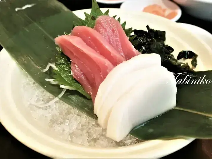 Fresh tuna and white fish sashimi served on ice with shiso leaves and seaweed.