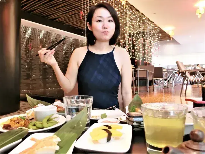 Woman dining at a restaurant with sushi and green tea, featuring decorative hanging lights in the background.