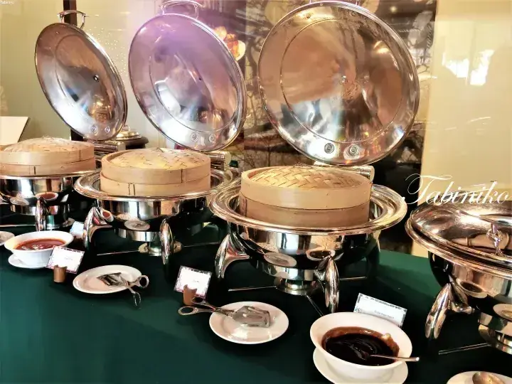 Buffet setup with bamboo steamers and silver chafing dishes on a green tablecloth.