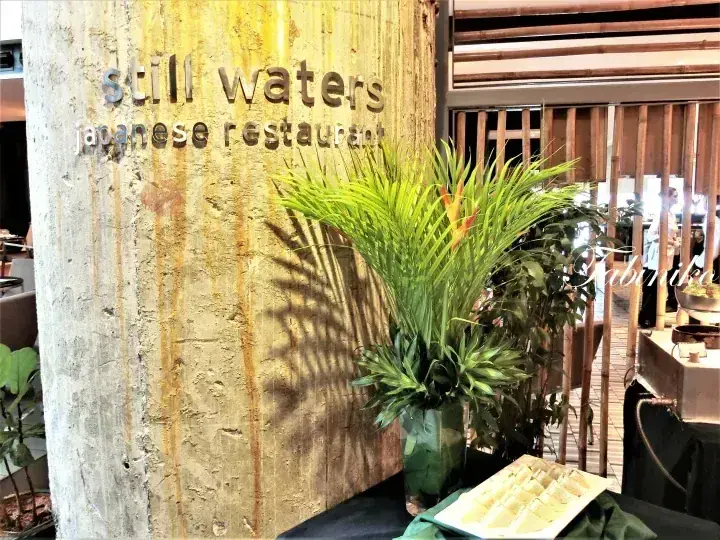 Still Waters Japanese Restaurant entrance with rustic concrete wall and tropical plants