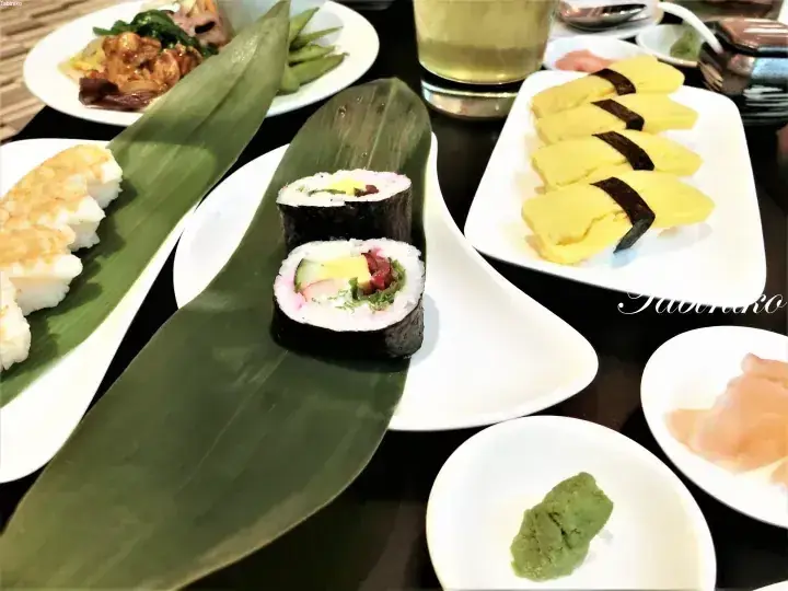 Assorted Japanese sushi and dishes served on white plates with banana leaves, including a maki roll and tamago nigiri.
