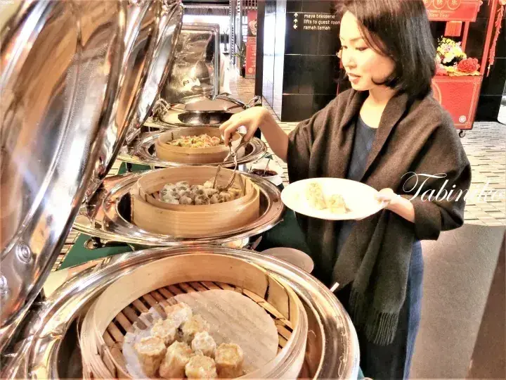 A woman selecting dim sum from bamboo steamers at a buffet station.