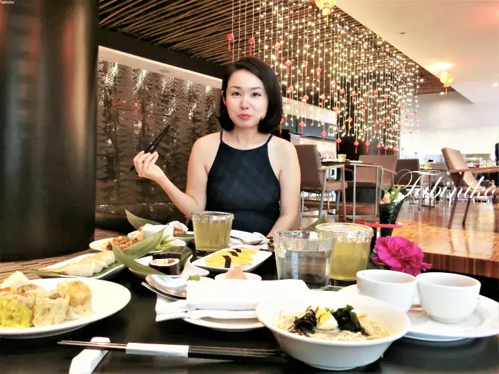 天井の装飾ライトが特徴的なレストランで、ディンサム料理が並んだテーブルで食事をする女性。