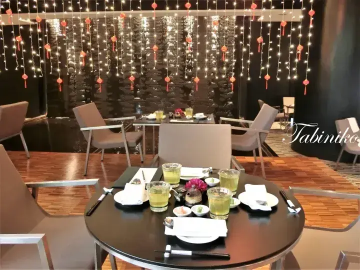 Elegant dining setup with drinks and appetizers on a round table, featuring a decorative water wall with hanging lights and lanterns.