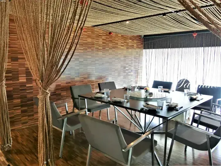 Modern dining room with a large table, grey chairs, and decorative rope curtains against a wood-paneled wall.