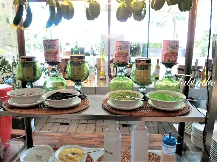 Buffet spread with Gold Coin beer glasses and bowls of food on a table near a window with hanging plants.