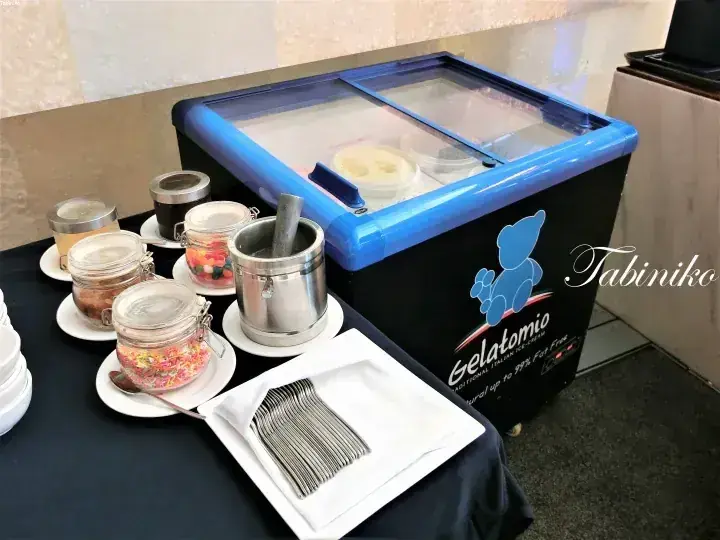 Gelatomio ice cream freezer with toppings and spoons at a buffet station