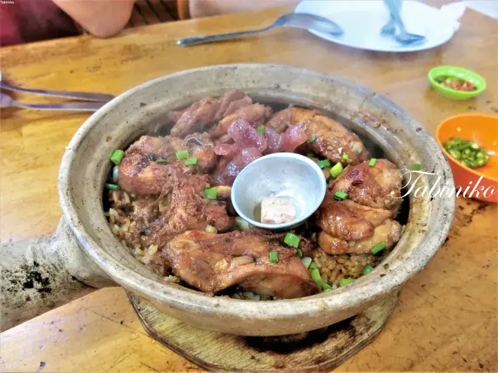 Chicken claypot rice served in a traditional clay pot with a small bowl of condiment on a wooden table.
