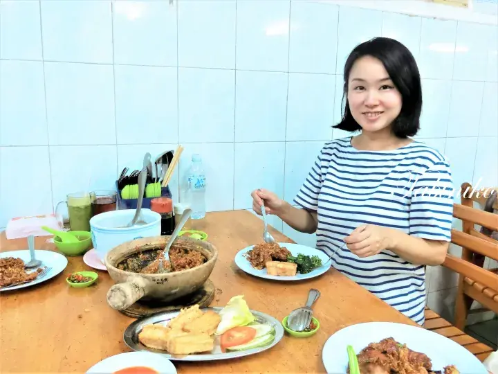 Woman enjoying a traditional Malaysian meal with claypot dishes at a local eatery.