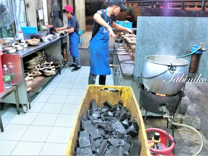 Chefs prepare Tabiniko dishes in an outdoor kitchen with a large pot and charcoal.