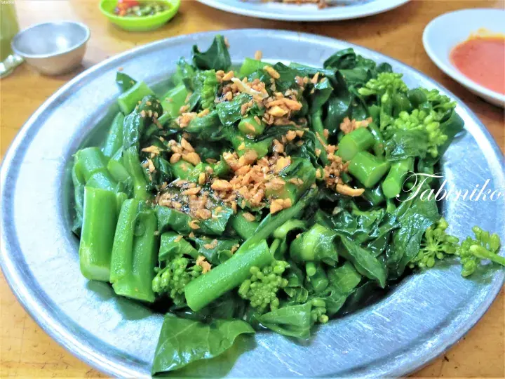 Stir-fried Chinese broccoli with garlic served on a metal plate at a Malaysian restaurant.
