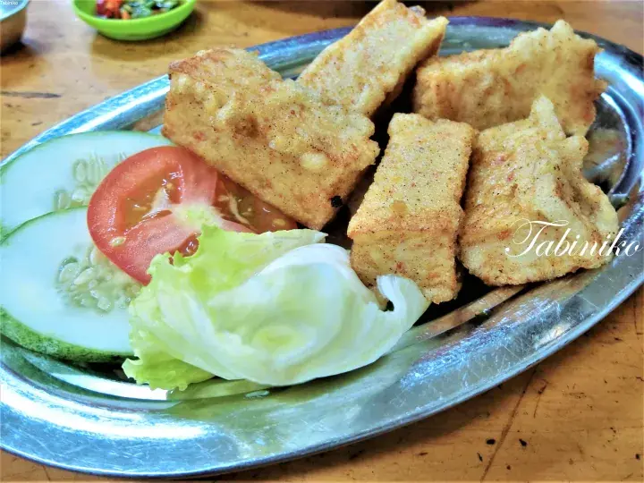 Golden fried tofu served on a metal plate with fresh cucumber, tomato, and lettuce.