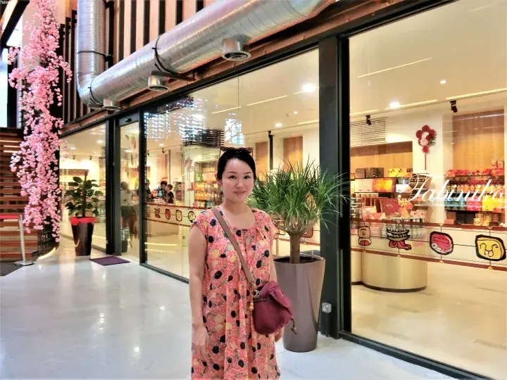 A woman stands smiling outside a modern shopfront with large glass windows and pink floral decorations.