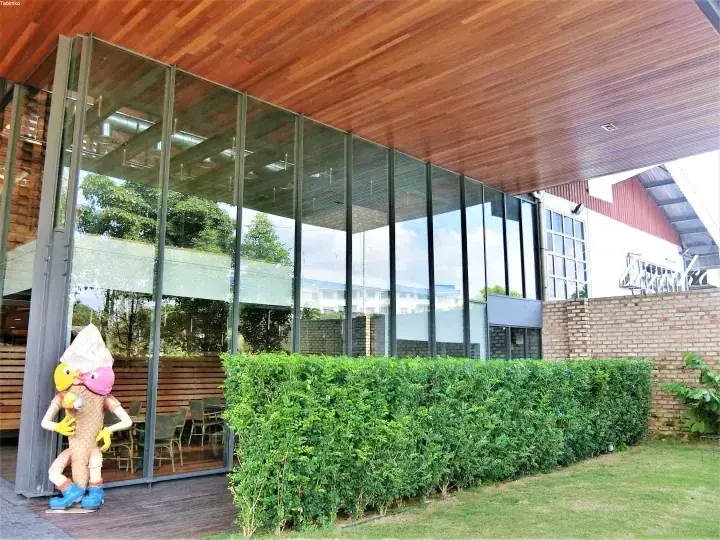 アイスクリームの像と緑に囲まれた、木製天井のモダンなガラス張りの建物。